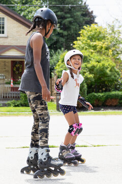 Teen teaching her young sibling to inline skate outside in the summer
