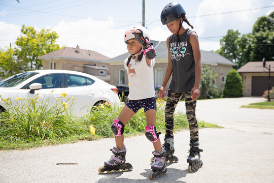 Teen teaching her young sibling to inline skate outside in the summer