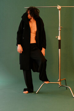 Stylish Man Posing in Black Coat Against Green Background