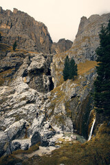 Scenic mountain landscape showcasing a waterfall surrounded by rocky terrain and coniferous trees in the early morning light