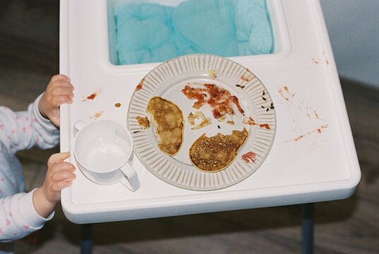 Baby girl reaches for the uneaten pancake at dining table.
