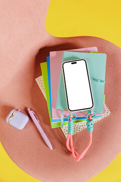 Smartphone with blank screen lying on stack of colorful notebooks