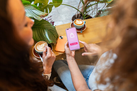 Two female friends using smartphone for online shopping in coffee shop