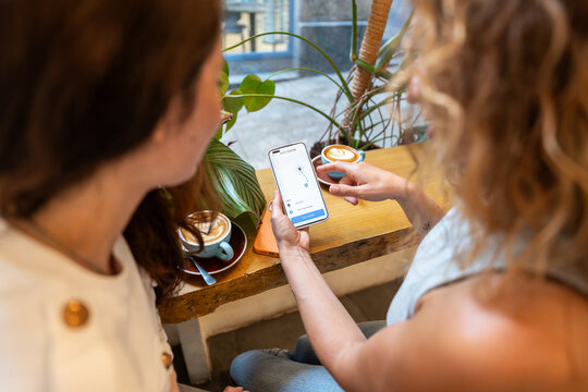 Two female friends using ride sharing app on smartphone in coffee shop