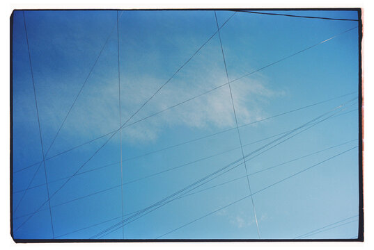 Clear blue sky with clouds and power lines crisscrossing 