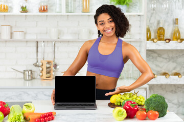 Ordering Food Online. Smiling fit black girl pointing at laptop with blank screen, staying cooking at home, mock up