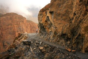 Obraz premium A man walking on An extremely rugged and rocky track among black and red rock mountains