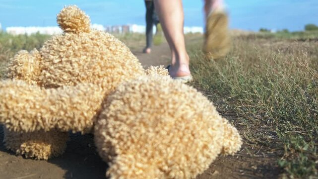 Person run after child on ground. A view of man run after little girl with teddy bear on the field. A concept of violence and kidnapping problems.