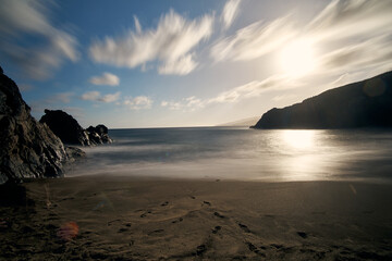 Beautiful sunset at a quiet beach with soft waves and rocky shoreline on a serene day