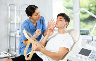 Obraz premium Client gazed into mirror, observing how female cosmetic doctor had rejuvenated his skin, and he felt youthful and confident in his appearance.