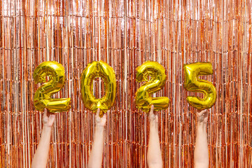 Hands holding gold 2025 balloons with tinsel backdrop

