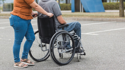 Close-up of woman pushing man with disability in a wheelchair. Personal assistance concept.