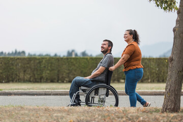 Smiling man, a wheelchair user, and his female assistant enjoying outdoor activity. Disability support concept.