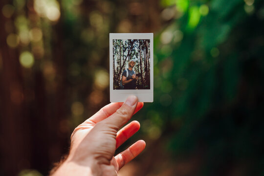 Hand holding polaroid photo of man in nature