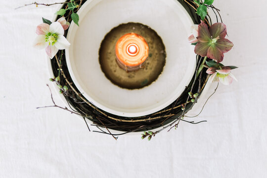 Candle surrounded by flowers in a white dish, close-up.