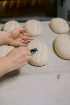 Hands scoring dough loaves before baking.