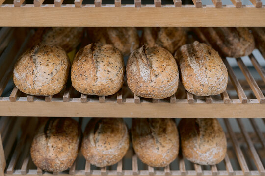 Multiple seeded bread rolls on a wooden bakery rack.