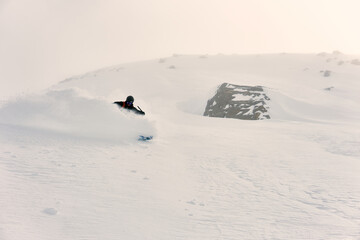 Snowboarder carving through fresh powder in a snow-covered mountainous region during winter