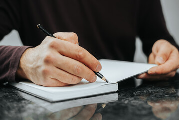 close up hand young man are sitting using pen writing Record Lecture note pad into the book on the table wood.