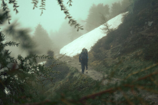 Hiker navigating a misty trail surrounded by snow and dense forest in a mountainous region