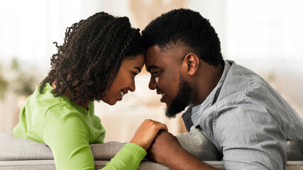 Obraz premium Tender Moment. Romantic Black Couple Bonding At Home, Holding Hands And Touching Foreheads, Relaxing On Couch Together