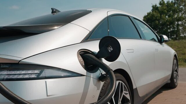 Electric car Supercharger station EV Car connected power cable on sea coast in warm light of lens flares at sunset. Car sharing commuter charging station  Alternative energy
