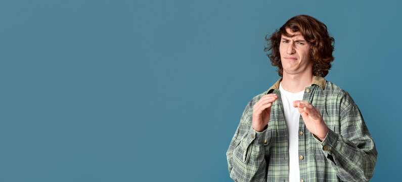Expressing disgust. Millennial guy with curly hair feeling repulsed on turquoise background