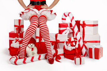 Christmas banner with young woman in a Miss Santa outfit with long legs in striped stockings and red heels surrounded by Christmas gifts.