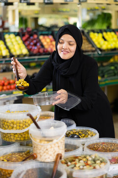 Asian girl in hijab buys pickled olives by weight in the supermarket