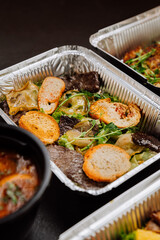 Gourmet salad with grilled beef, fresh greens, and crispy toast, served in container for takeout
