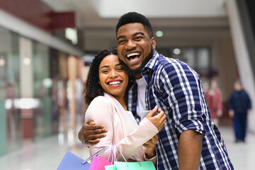 Obraz premium Happy Buyers. Cheerful African American Couple With Shopper Bags Hugging In Department Store After Successful Shopping