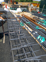 Construction site with steel rebar structure for concrete reinforcement being assembled by workers in safety gear. Various construction materials and equipment in background.