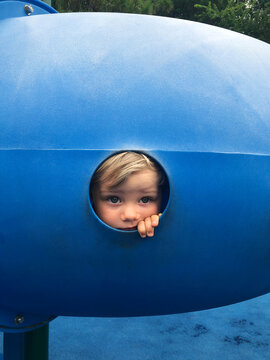 Toddler boy peers out of playground tube.