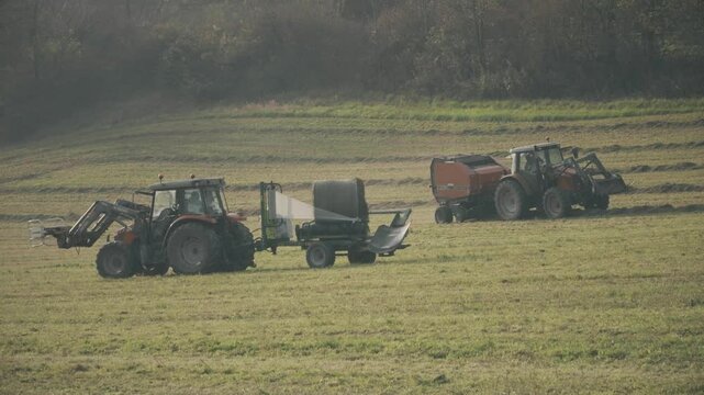 Two tractors with hay baler and haystack packaging equipment in the field, France