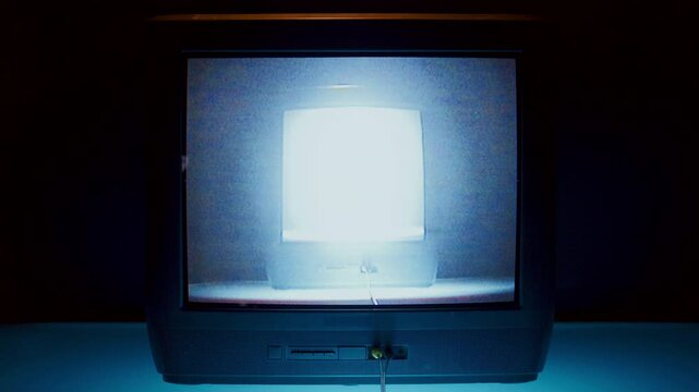 Retro TV monitor showing no signal blue screen, then screen recursion effect, with brightly glowing image of another screen displayed within its own display in dark room. Close-up shot