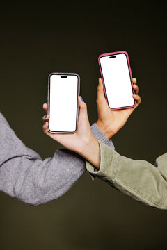 Two women showing smartphones with white screen on dark background