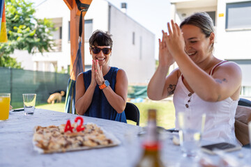 Two women celebrating birthday with cake at outdoor party