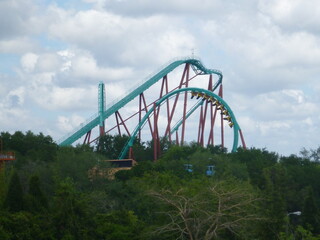 Blue green red rollercoaster with greenery and vegetation, cloudy sky
