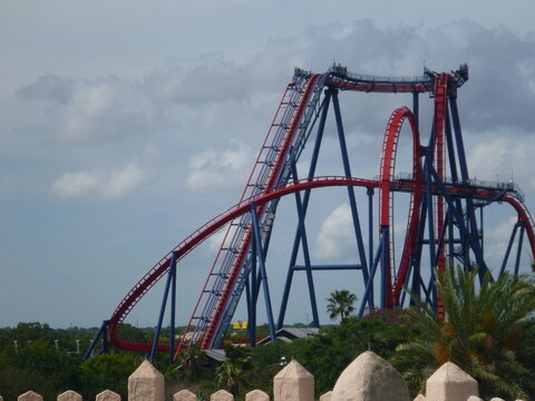 Large red and blue roller coaster in Florida, USA. With vegetation surrounding in foreground and cloudy sky