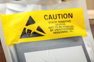 Yellow caution label on anti-static packaging for electronic components. Close-up macro shot.