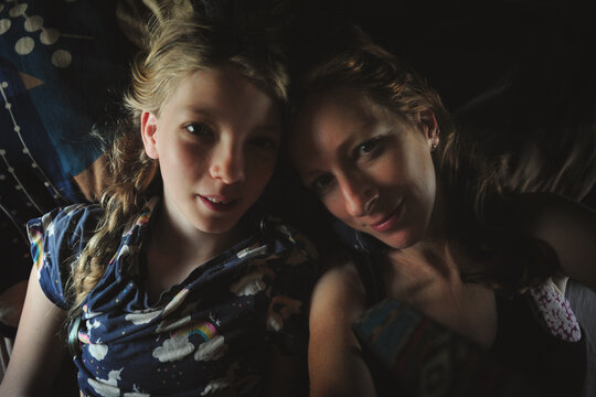 a woman and her daughter lie in bad for a selfie