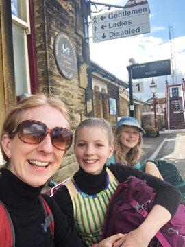 A mum and 2 daughters wait for a train in England