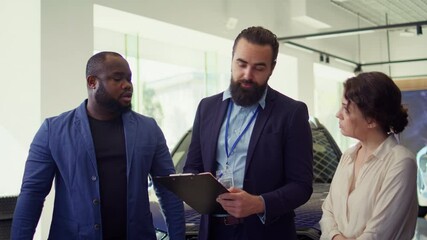 Friendly car salesman showcasing dealership vehicles to clients, explaining their features and warranties. Agent helping customers choose automobile, comparing competitive models, camera B