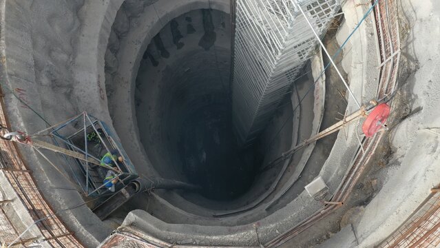 Workers descending into a subway construction shaft with a crane