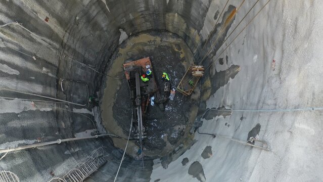 Work machine and workers inside underground subway well construction