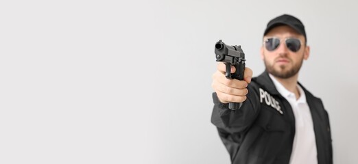 Male police officer with gun on light background with space for text