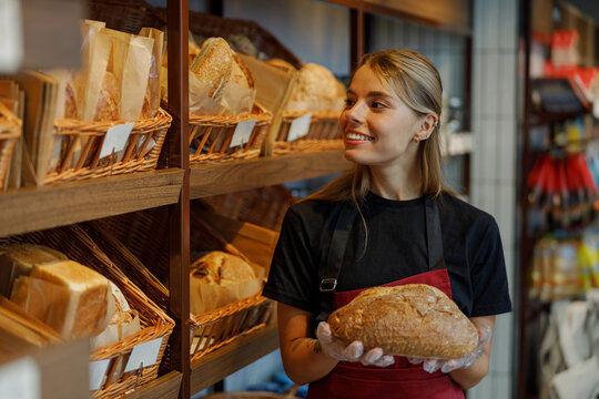 A female baker truly enjoys her time spent in the cozy bakery, proudly holding freshly baked artisan bread