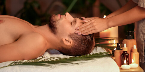 Young man getting treatment head massage on couch in dark spa salon