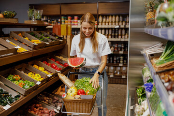 A cheerful woman takes delight in selecting a variety of fresh fruits and colorful vegetables at a grocery store