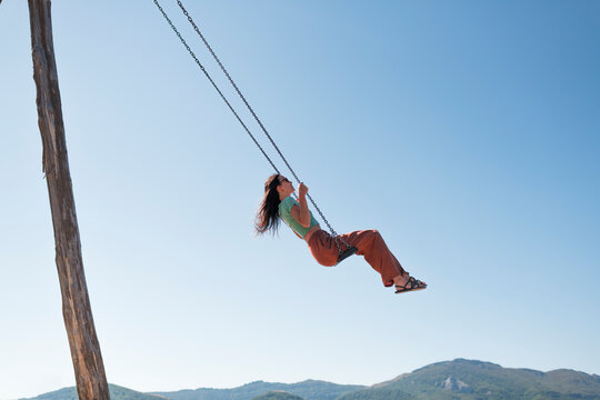 Cheerful woman swinging in blue sky